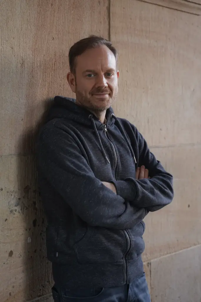 Dirk lehnt an Wand mit verschränkten Armen